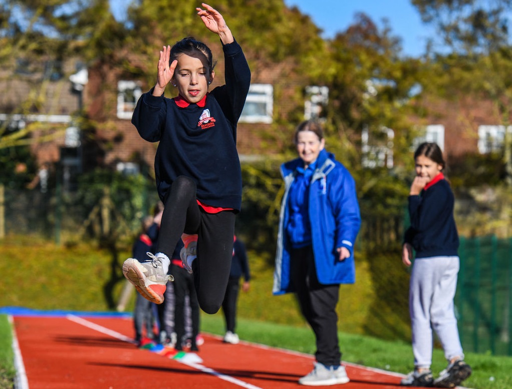 Child long jumping while being watched by coach