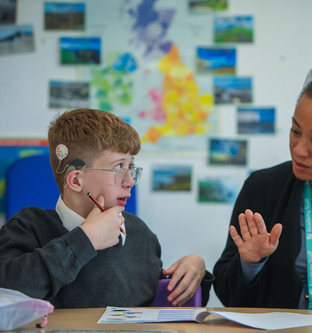Teacher explains something to boy with hearing aid implant