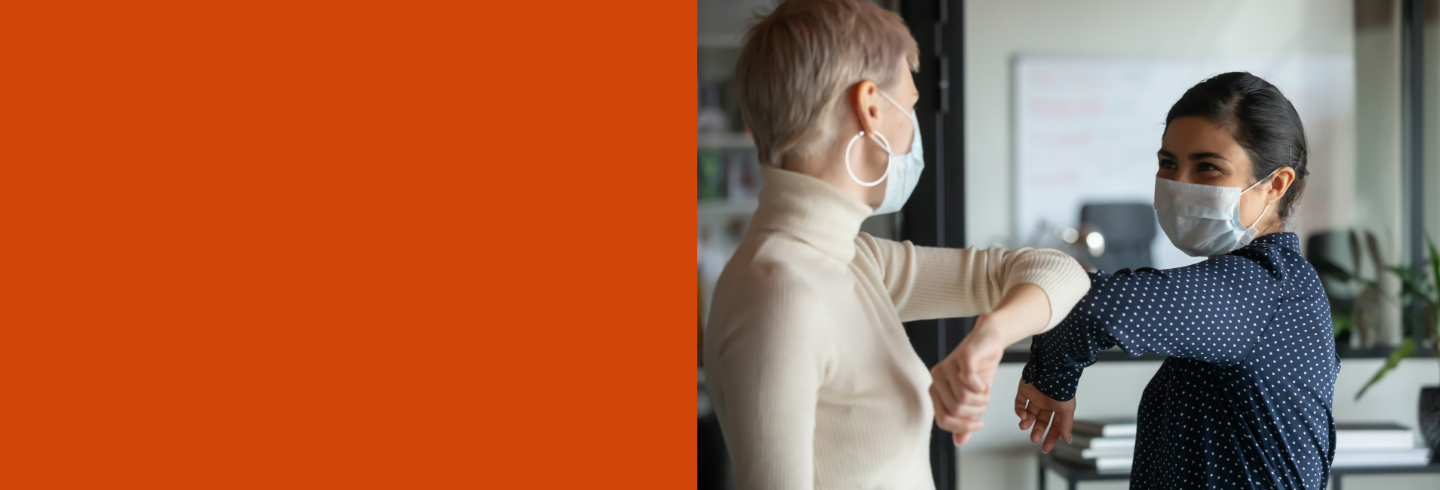 two women wearing masks and elbow bumping 