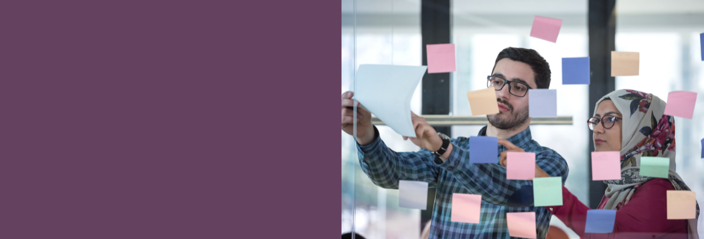 Two team members standing at glass office wall with coloured sticky notes 