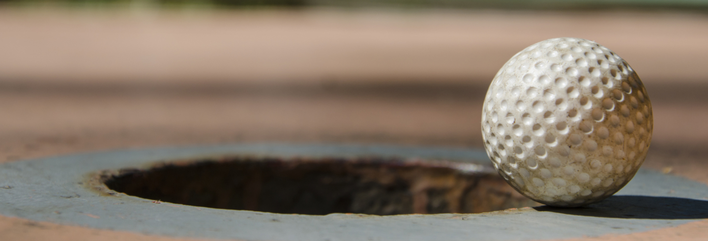 Golf ball teetering on the edge of the hole