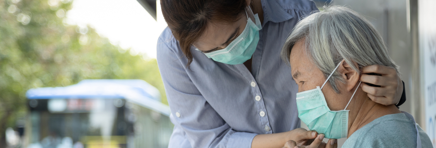 young women helping elderly man put on protective mask
